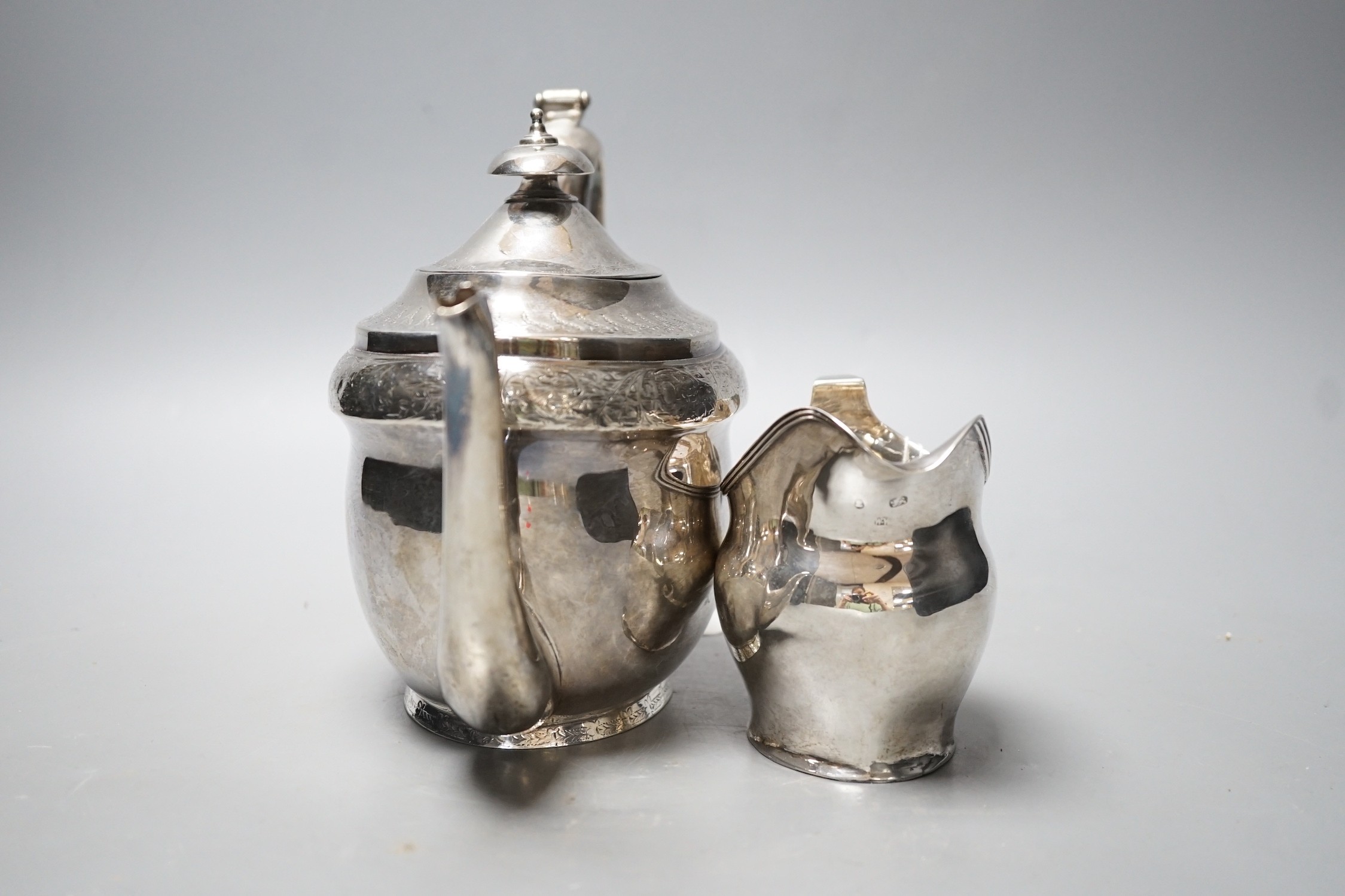 A George III engraved silver oval teapot on stand, Hannah Northcote? London, 1804 and Georgian silver cream jug, marks rubbed, gross 24.8oz.